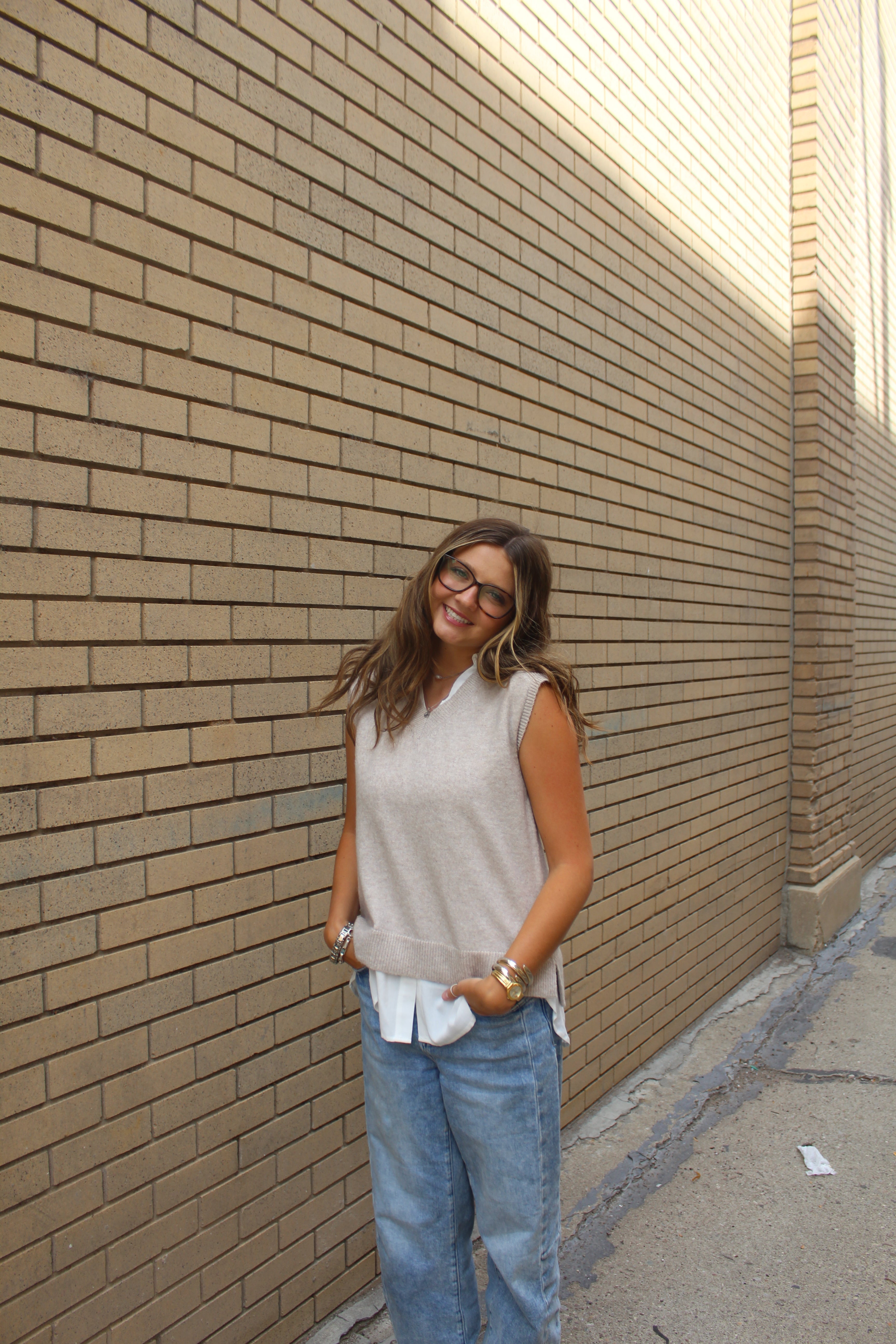 Lady wearing a sweater vest with jeans standing near a brick building