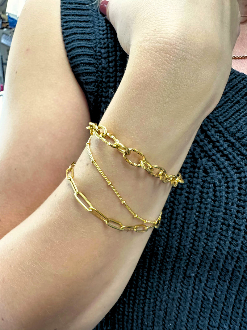 3 dainty gold bracelets on a woman's arm.