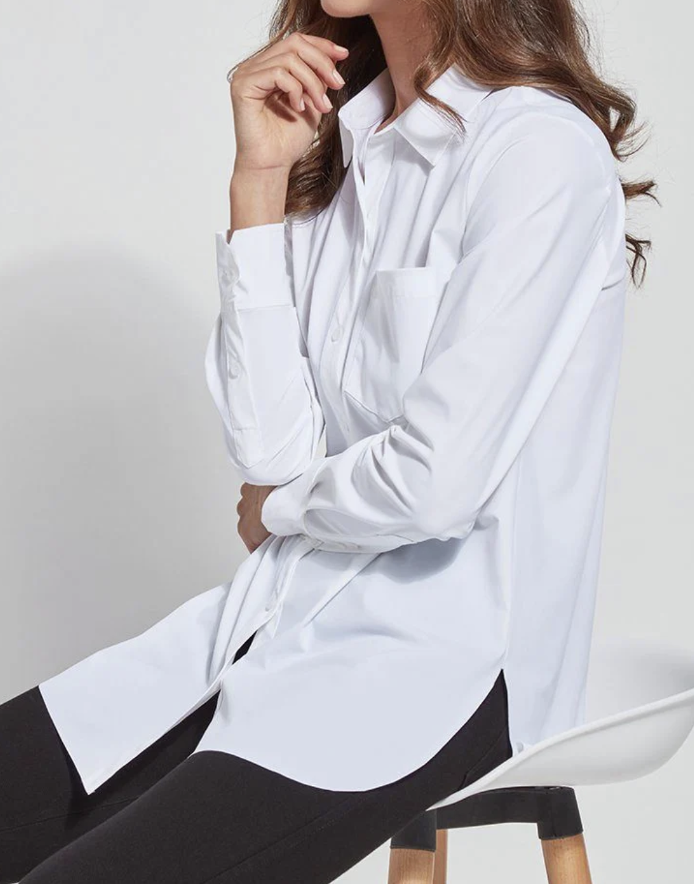 Woman wearing a white shirt with buttons up and down, sitting on a chair.