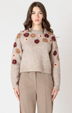 A cozy oat colored knit sweater with fall colored flowers stitched into the arms and upper bodice.