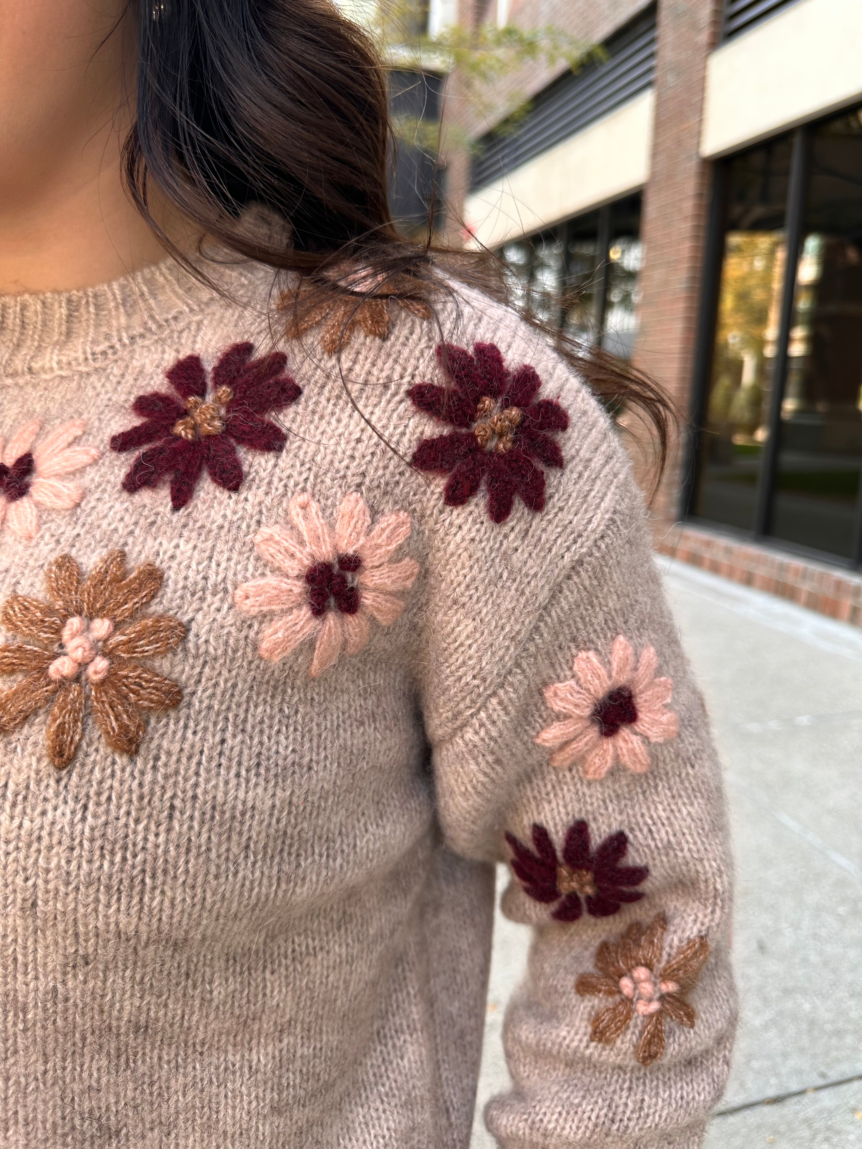 A cozy oat colored knit sweater with fall colored flowers stitched into the arms and upper bodice.