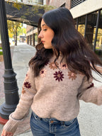 A cozy oat colored knit sweater with fall colored flowers stitched into the arms and upper bodice.