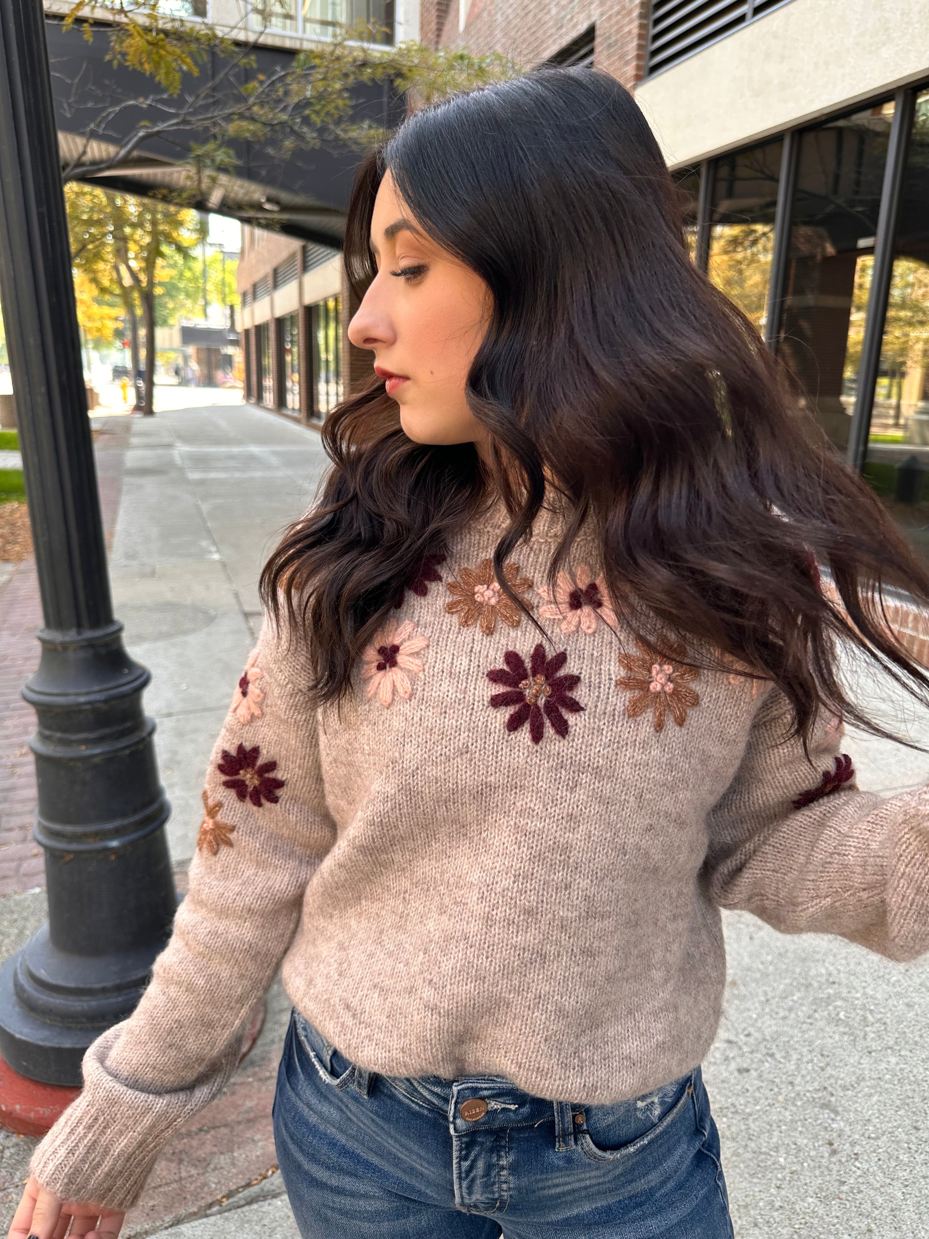 A cozy oat colored knit sweater with fall colored flowers stitched into the arms and upper bodice.