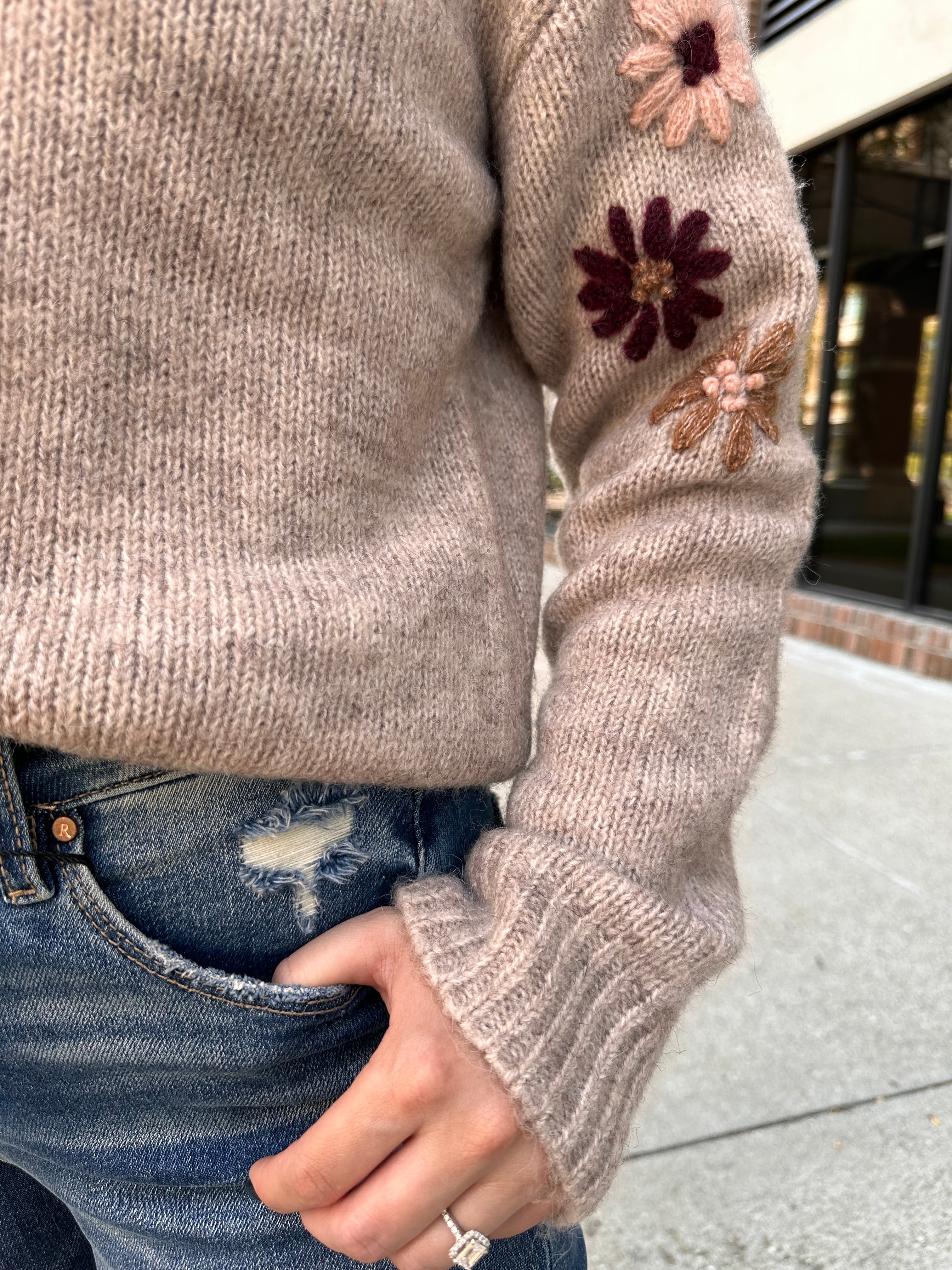 A cozy oat colored knit sweater with fall colored flowers stitched into the arms and upper bodice.