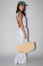 Woman wearing a light blue striped dress with cut-out design, holding a woven bag against a plain background.