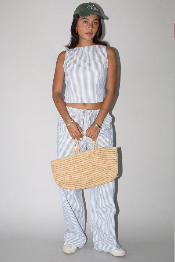 Person wearing a light blue striped outfit with a straw bag against a plain background