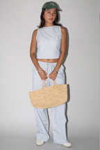 Person wearing a light blue striped outfit with a straw bag against a plain background