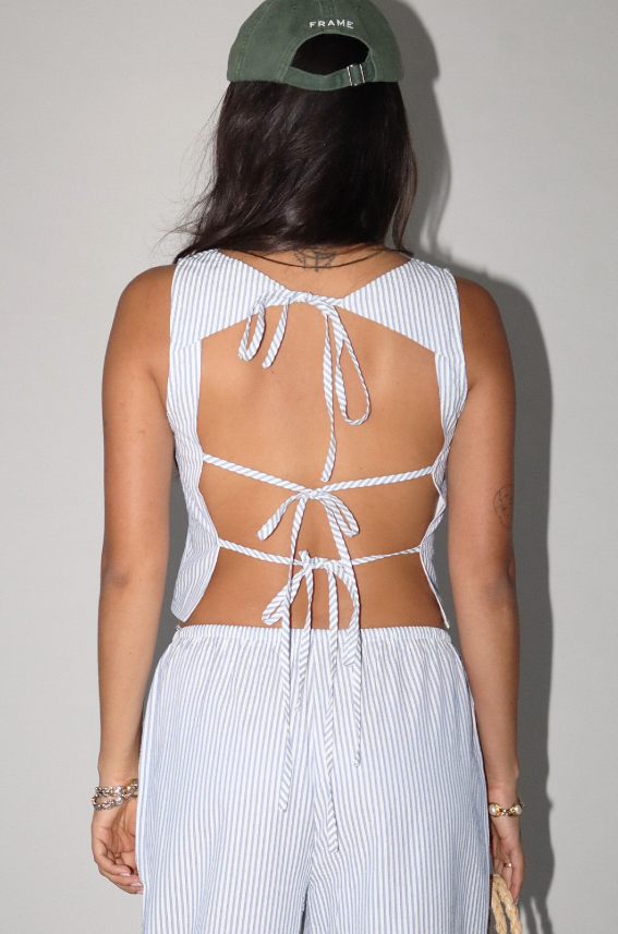 Person wearing a white open-back top and light-colored pants against a plain background