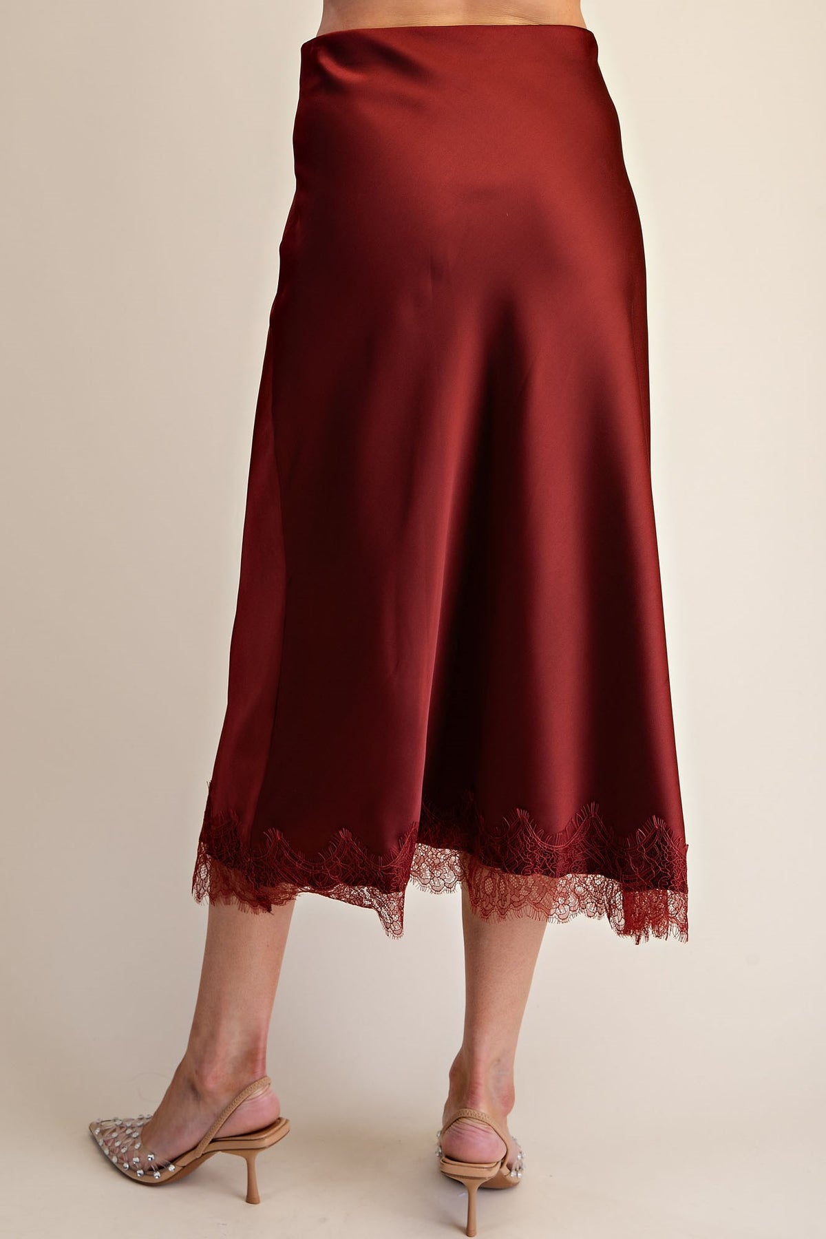 A dark red satin midi skirt with a lace hem, shown on a model from the back against a plain beige background.