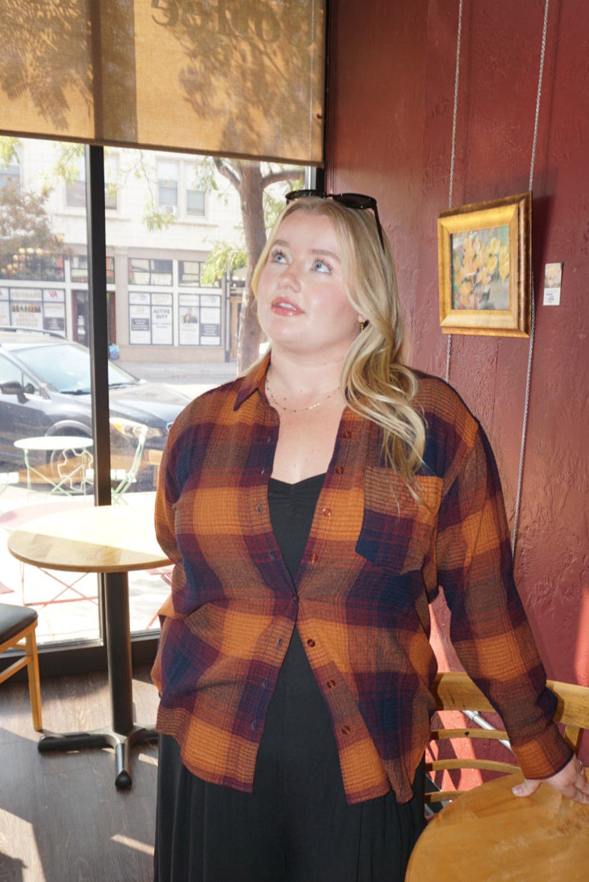 A flannel style button up shirt, with orange, blue, and red autumnal colors. 