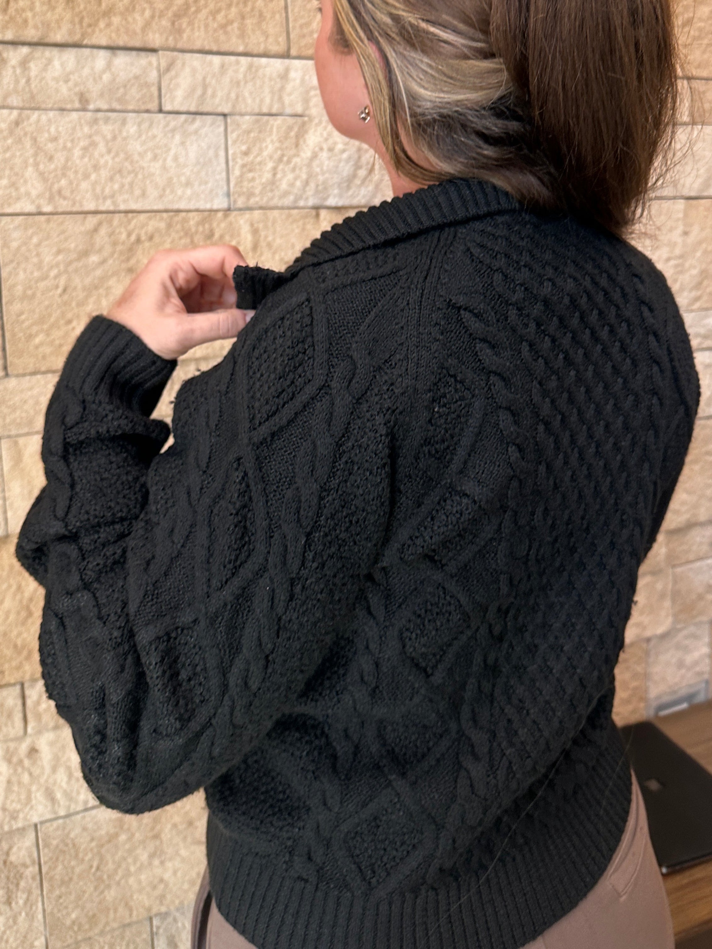 Person wearing a black cable knit sweater on a wooden floor