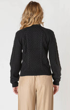 Person wearing a black cable knit sweater and beige pants on a white background