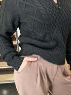 Person wearing a black cable knit sweater and beige pants on a wooden floor.