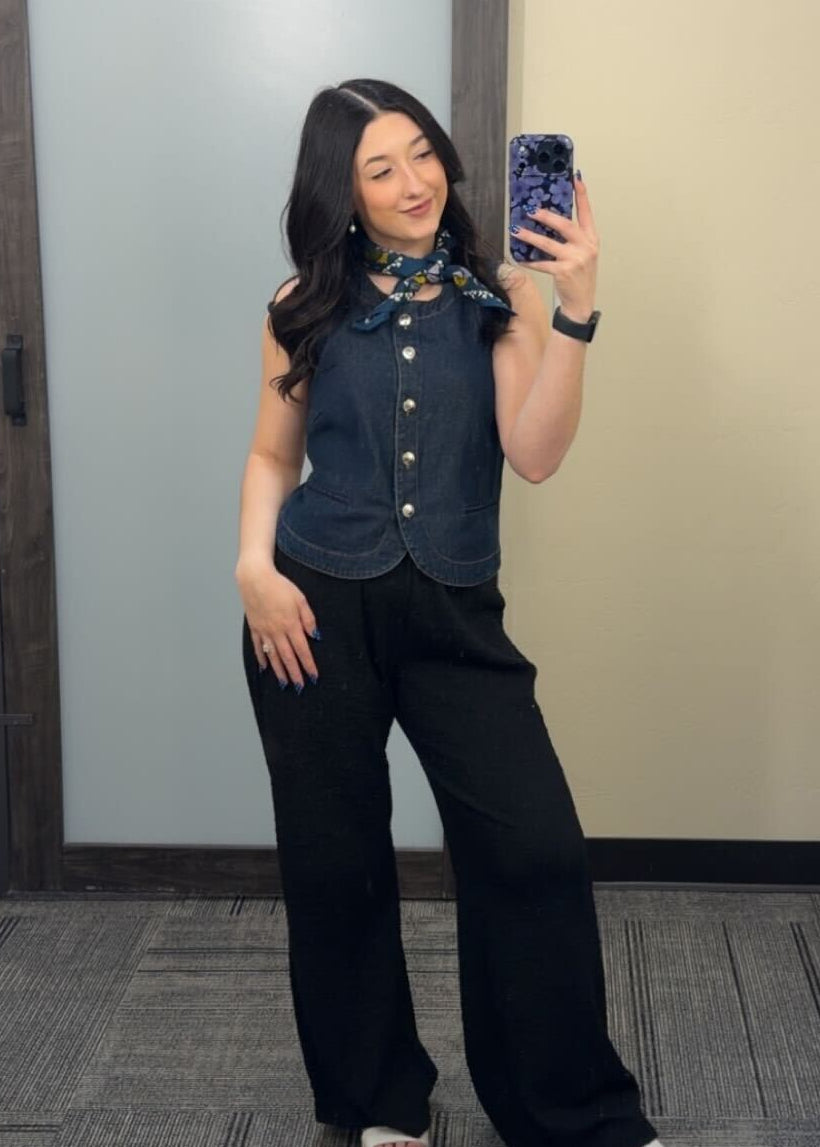 A woman taking a mirror selfie wearing a dark denim top with black pants.