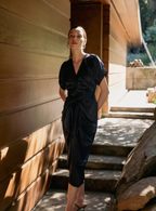Woman wearing a satin dress with buttons and tie in the front standing outdoors.