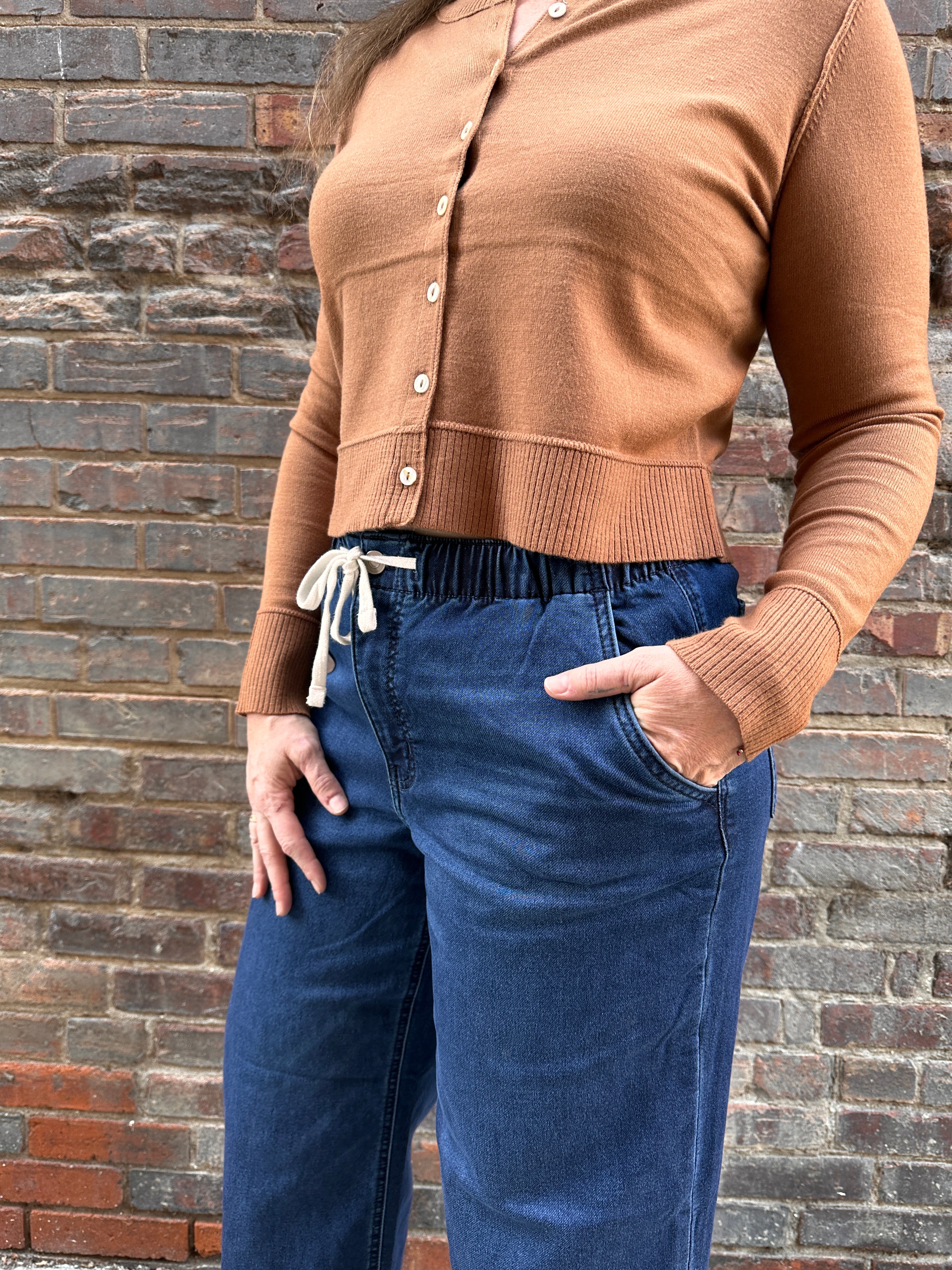 Light brown cardigan with drawstring pants on a woman in front of a brick wall