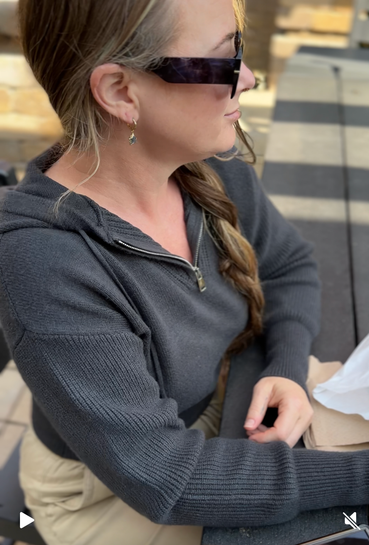 Person wearing sunglasses with a blurred face, sitting outdoors.