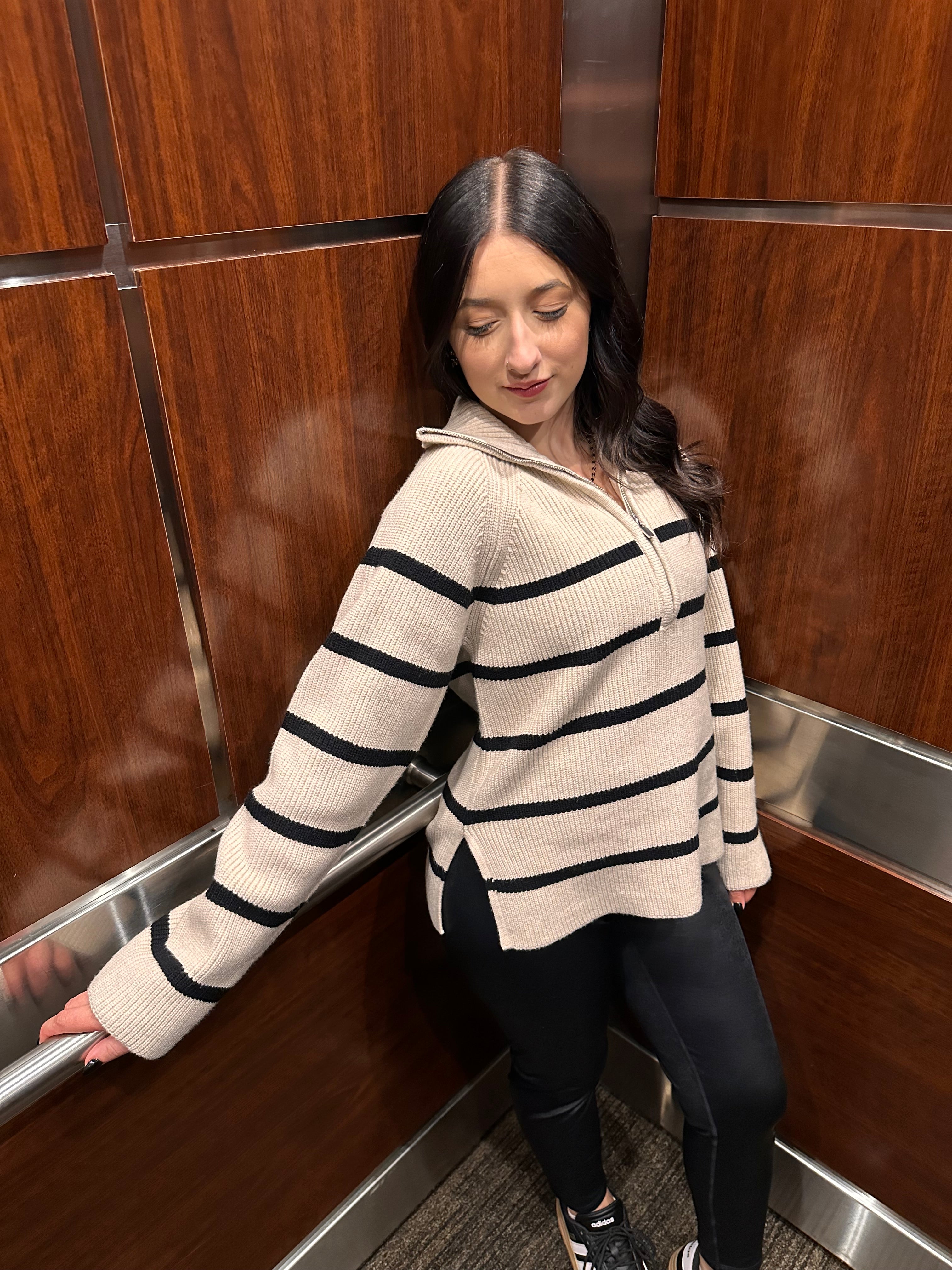 A cozy cream sweater with horizontal black stripes, and a half zipper, and a collar.