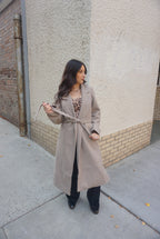 A beautiful and timeless oat colored coat, with a tie waste, a trench like lapel, and pockets.