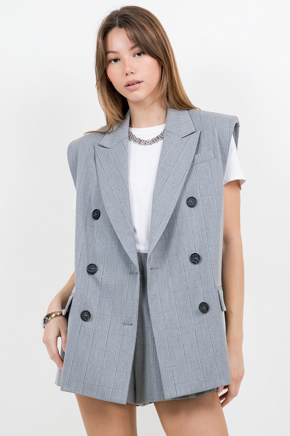 A grey suit jacket style vest with double-breast buttons, slightly padded shoulders, and pinstripe details. 