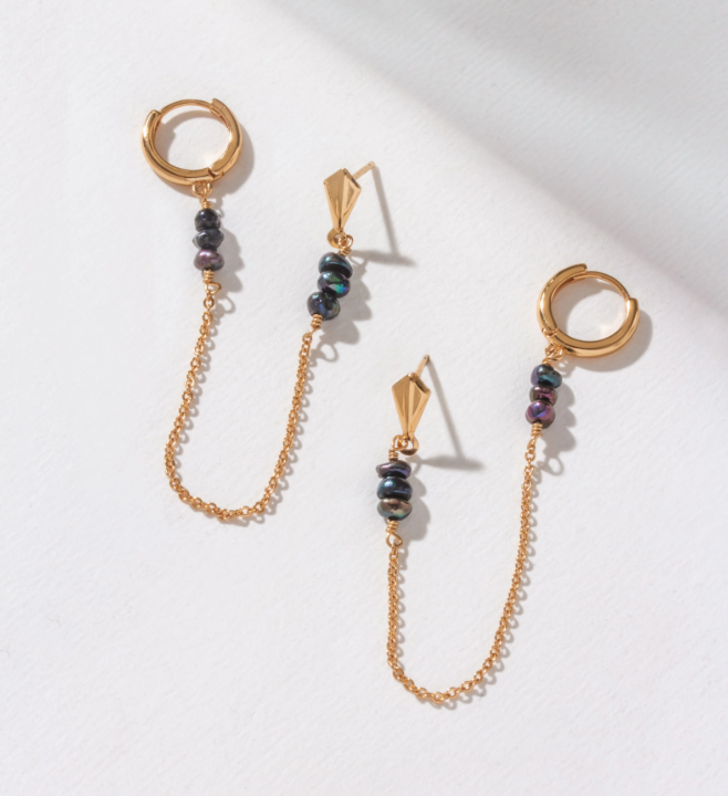 Gold earrings with a hoop connecting to a post with a gold chain adorned with small stones.