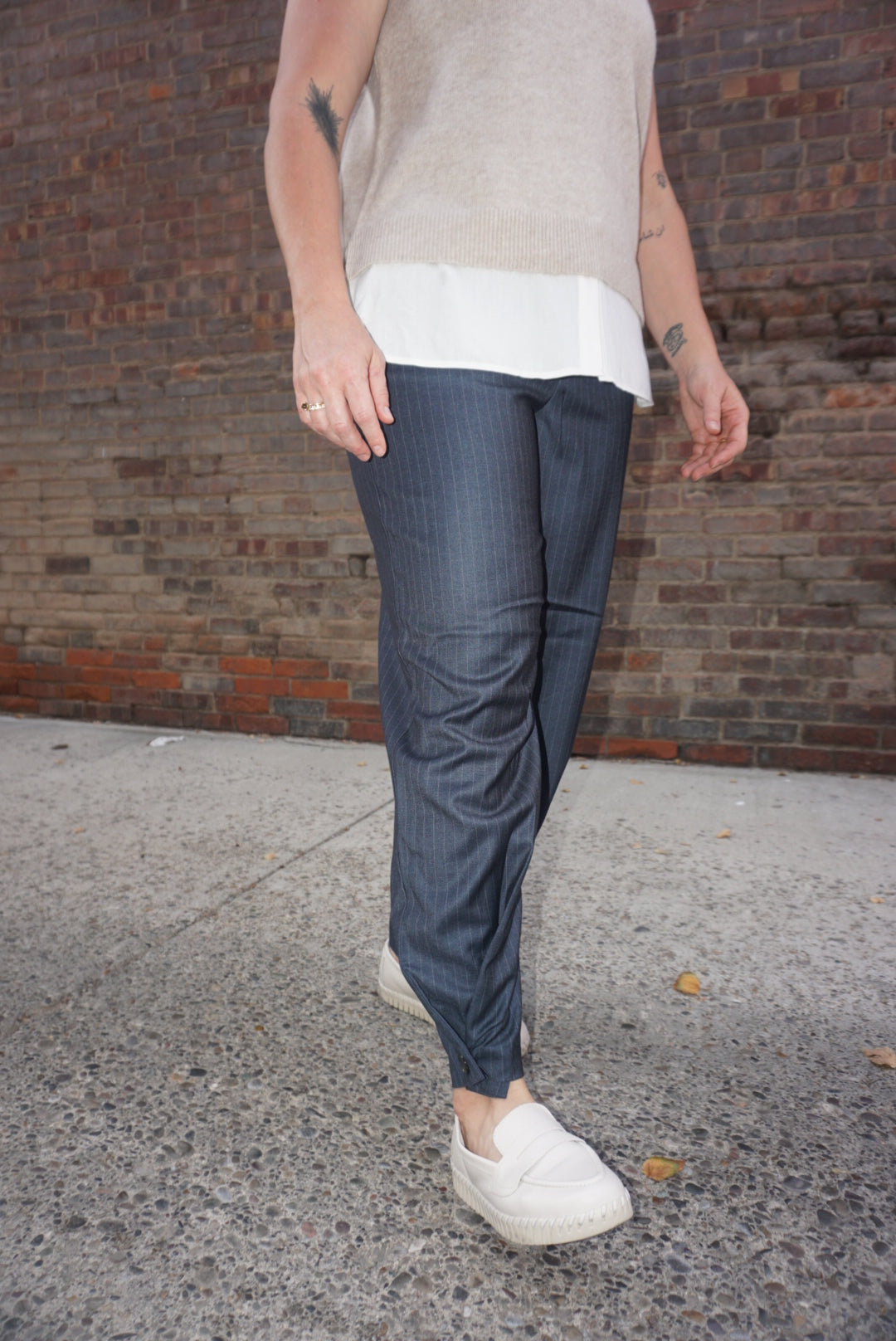 A sharp pair of trousers, in a dark blue pinstripe material, with a button on the hem, allowing you to choose how to style these pants.