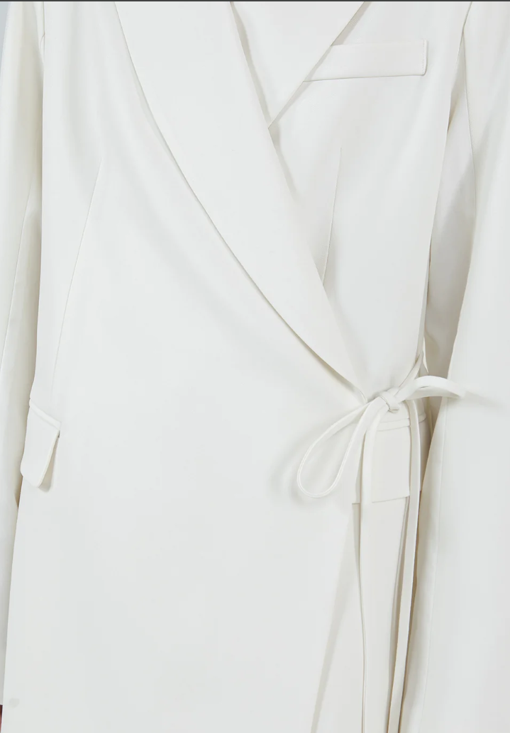 Close-up of a white blazer with a tie detail on a light gray background