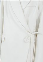 Close-up of a white blazer with a tie detail on a light gray background