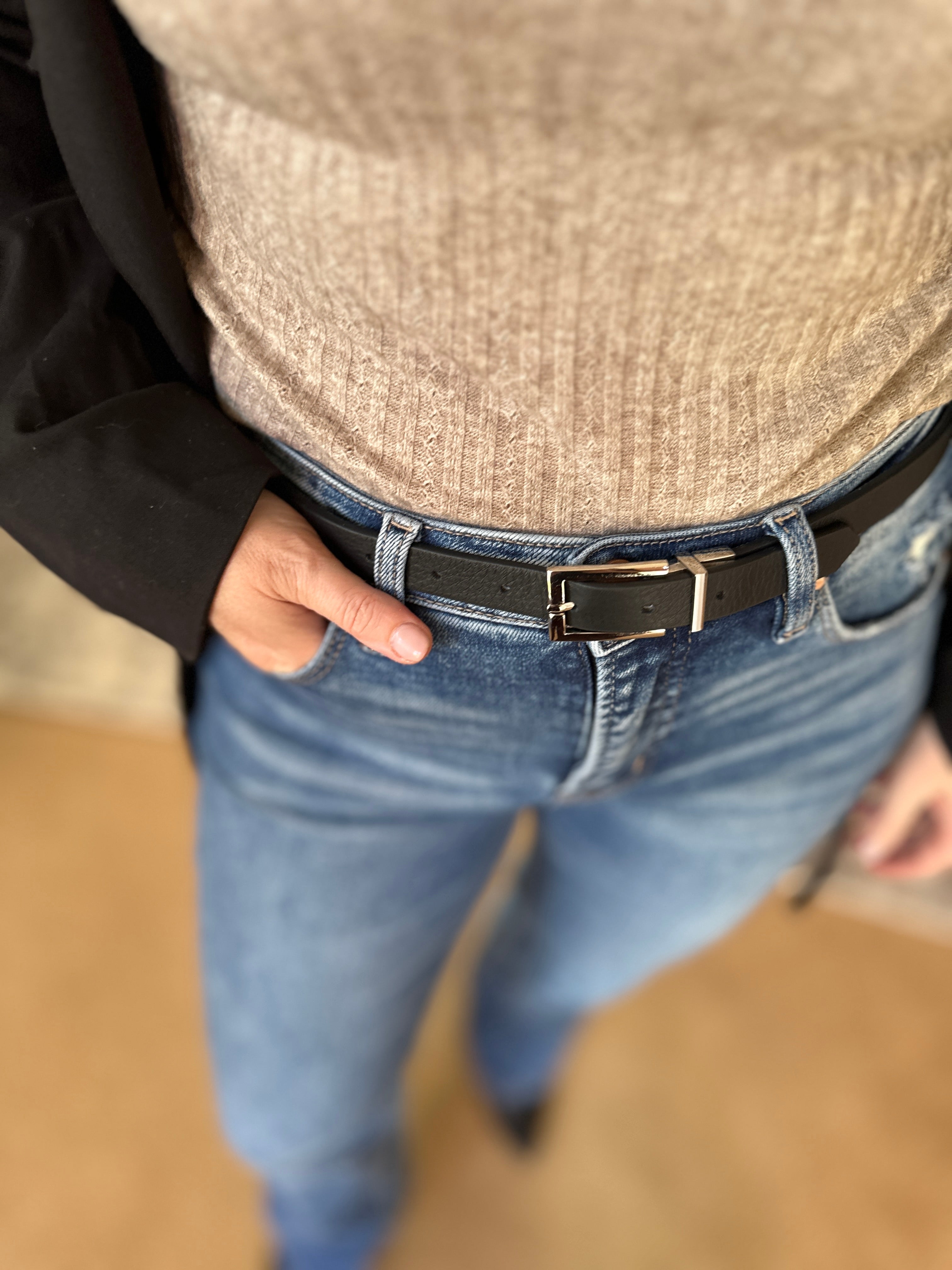 Person wearing a beige shirt, blue jeans, and a black belt with a blurred background