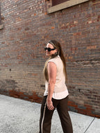 A woman wearing a sweater vest and pants with a stripe down the side walking on a sidewalk with a brick wall in the background