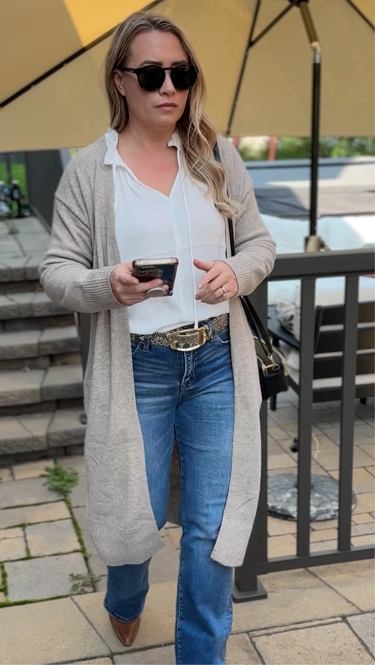 Woman in casual outfit with sunglasses and a phone, standing outdoors.