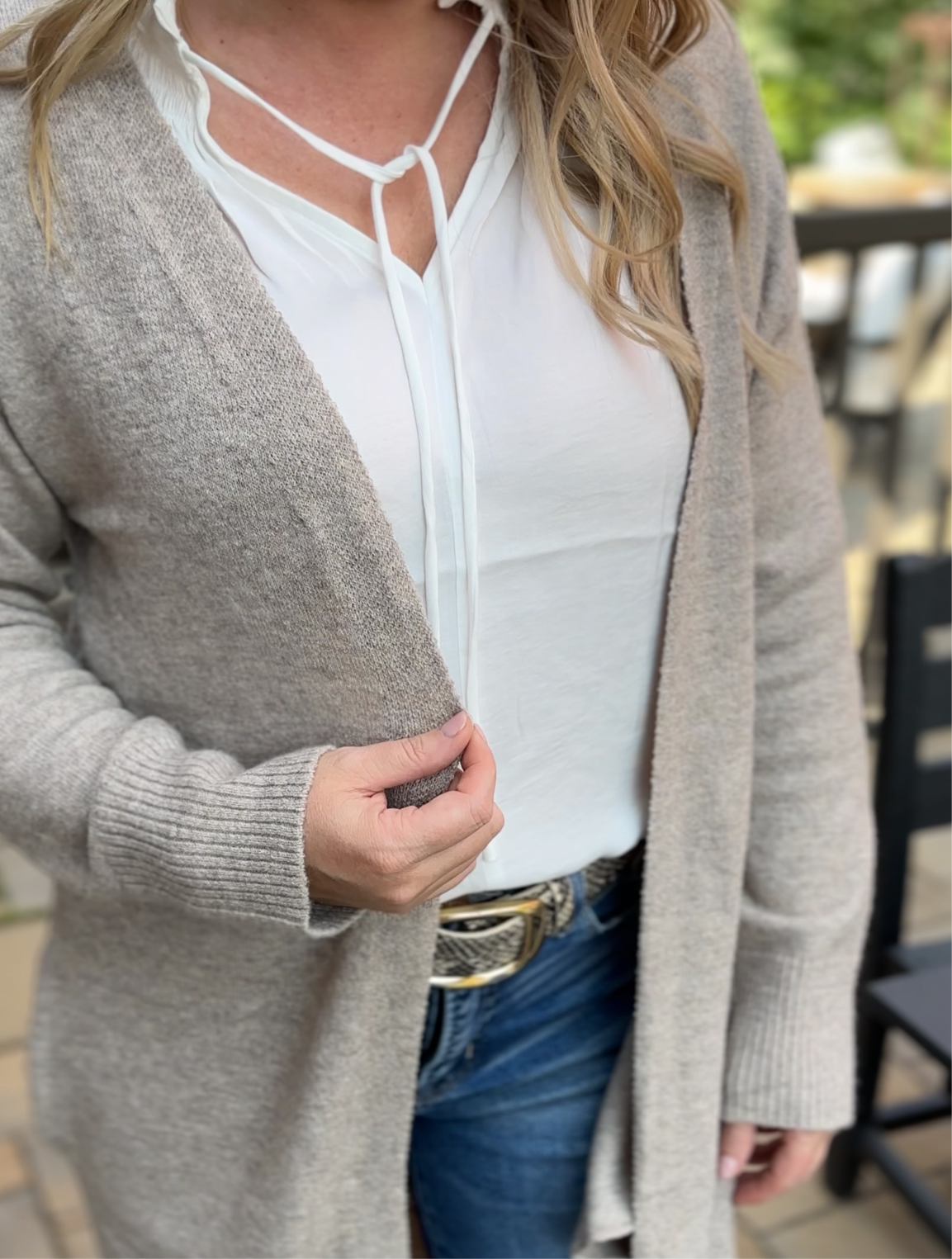 Person wearing a oat colored cardigan over a white top with blue jeans outdoors.