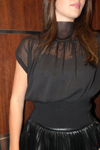 A chic black chiffon top with a high neck line, cap sleeves, and gathered waist. 