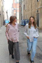 Two people standing on a sidewalk with a building in the background, one wearing a rose vertical striped button up and the other wearing a black and white vertical striped button up. 