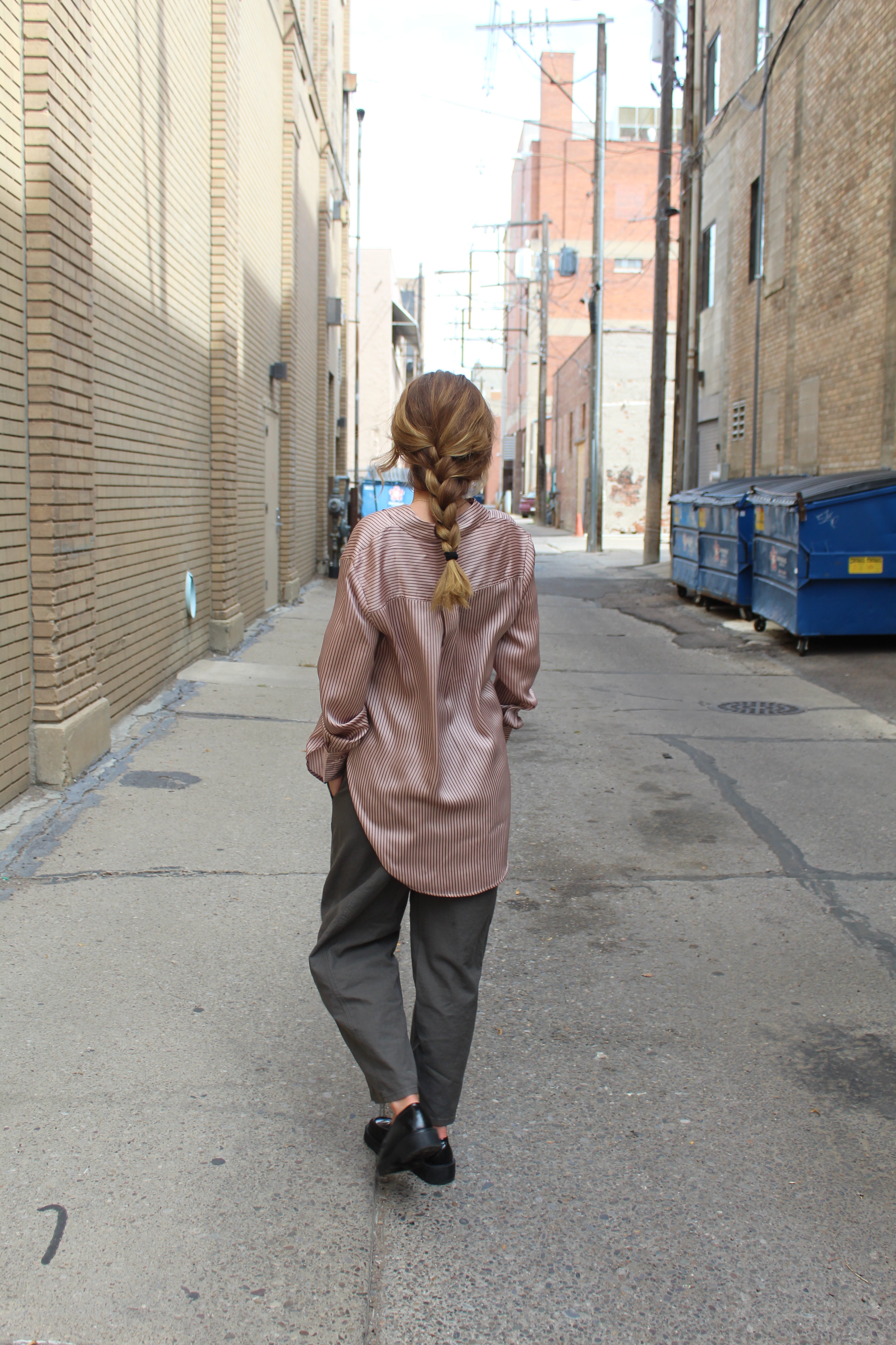Person wearing a rose vertical striped button down that has reflective and glossy texture and covers her bottom.