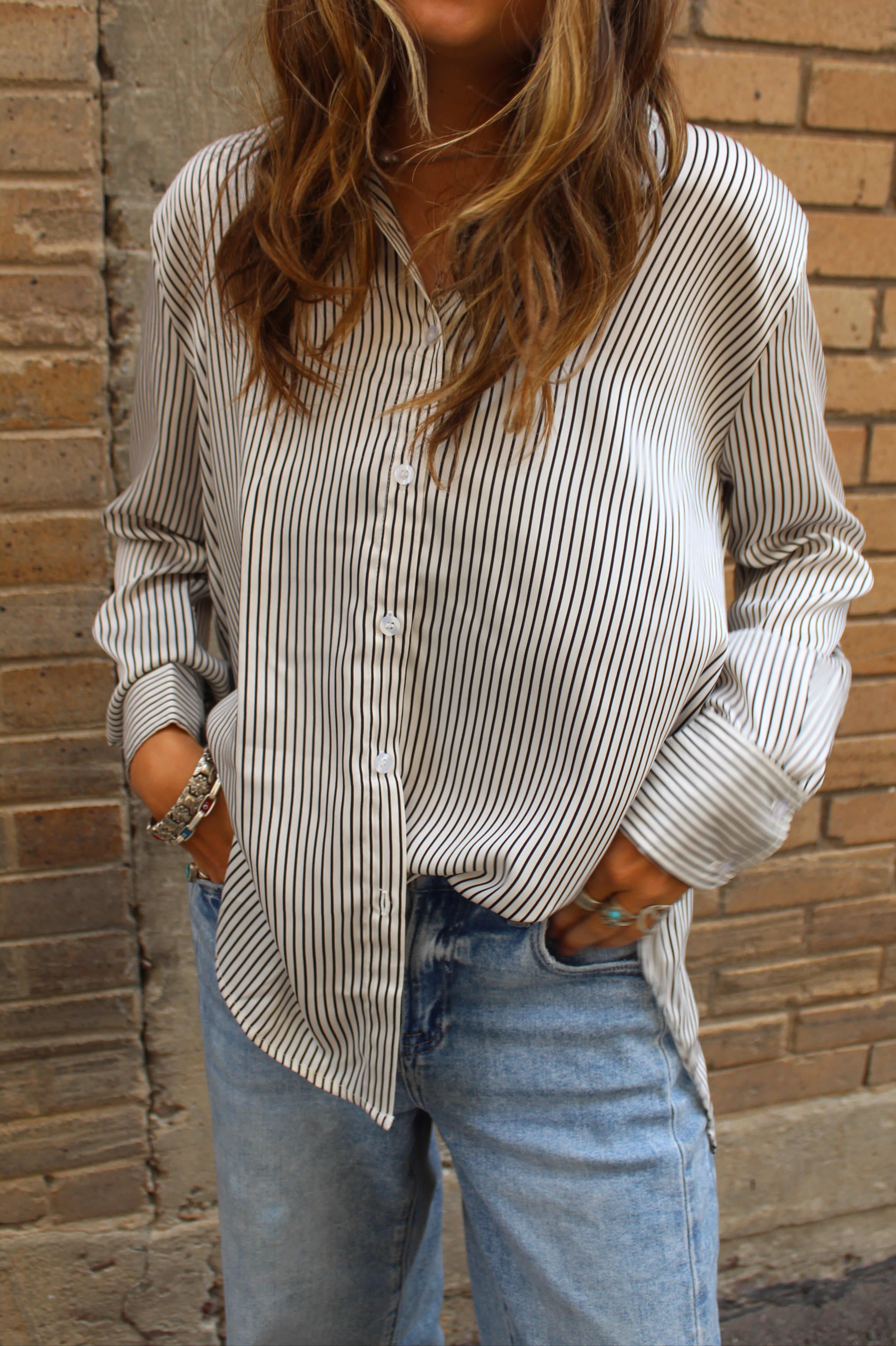 Person wearing a striped shirt and jeans against a brick wall