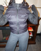 A black puffer jacket with a hood, and thick, stretchy, knitted sleeves.