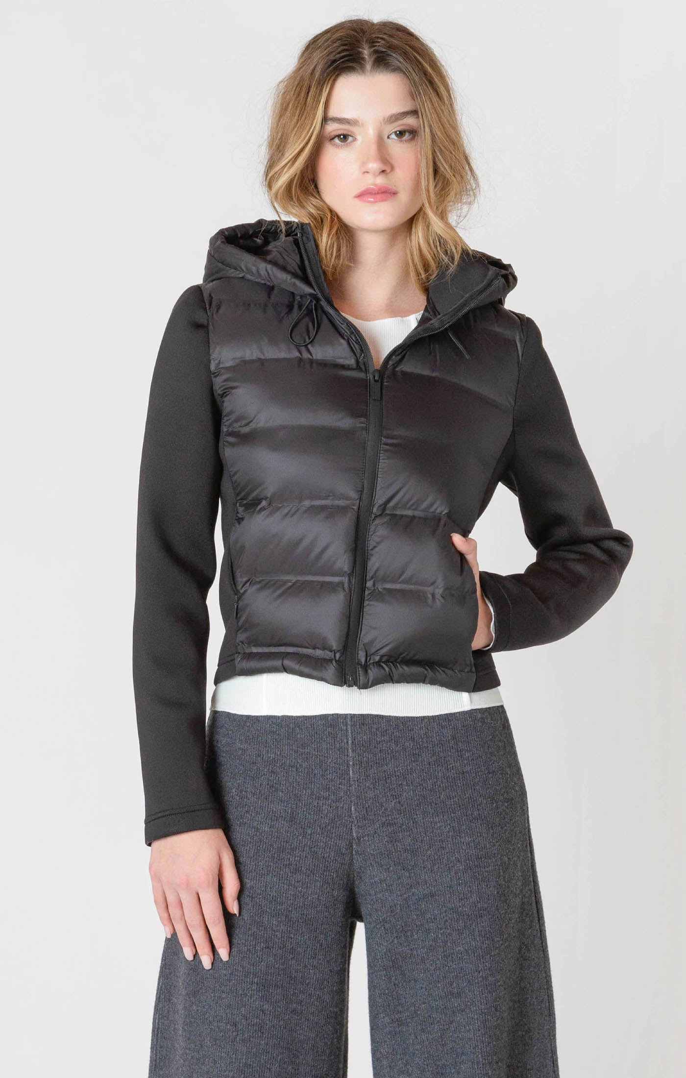 A black puffer jacket with a hood, and thick, stretchy, knitted sleeves.