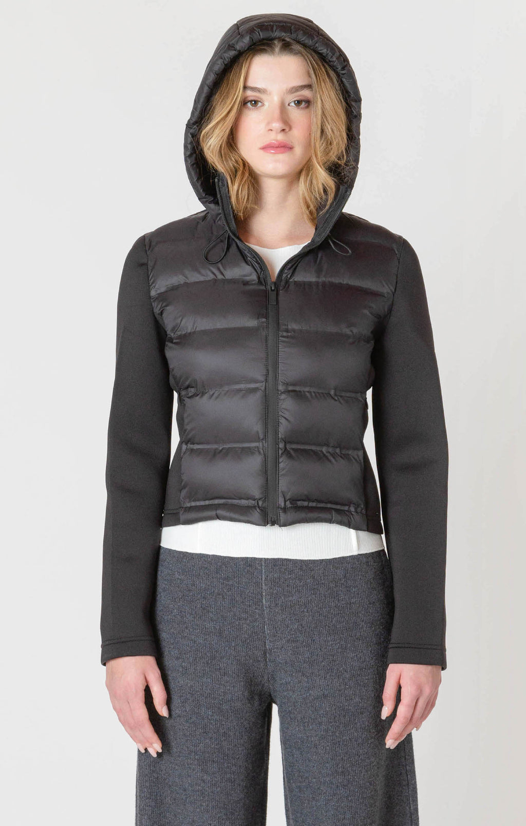 A black puffer jacket with a hood, and thick, stretchy, knitted sleeves.
