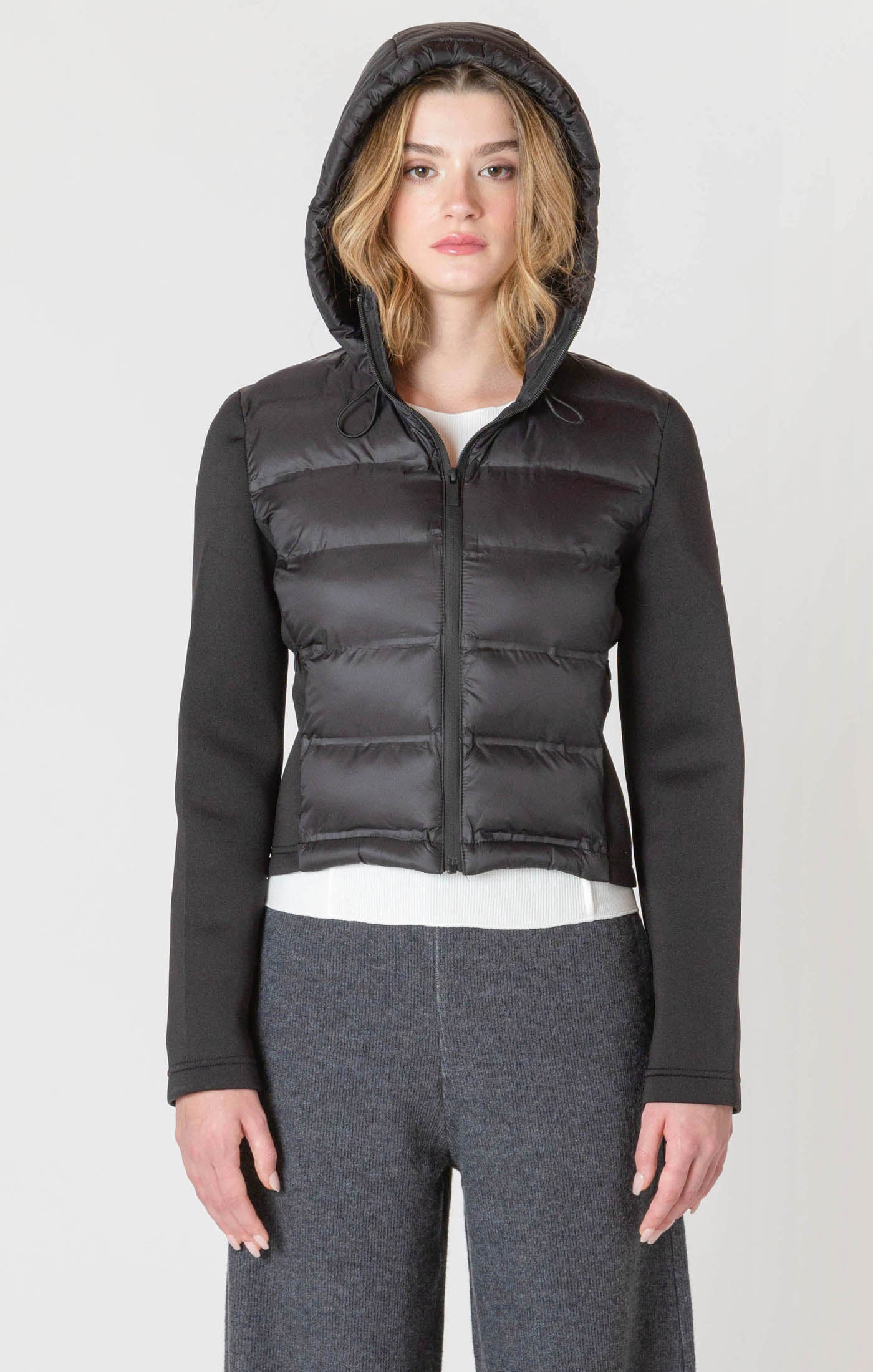 A black puffer jacket with a hood, and thick, stretchy, knitted sleeves.