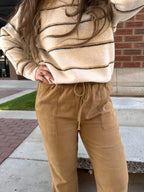 Person wearing a beige striped sweater and tan pants standing on a sidewalk.