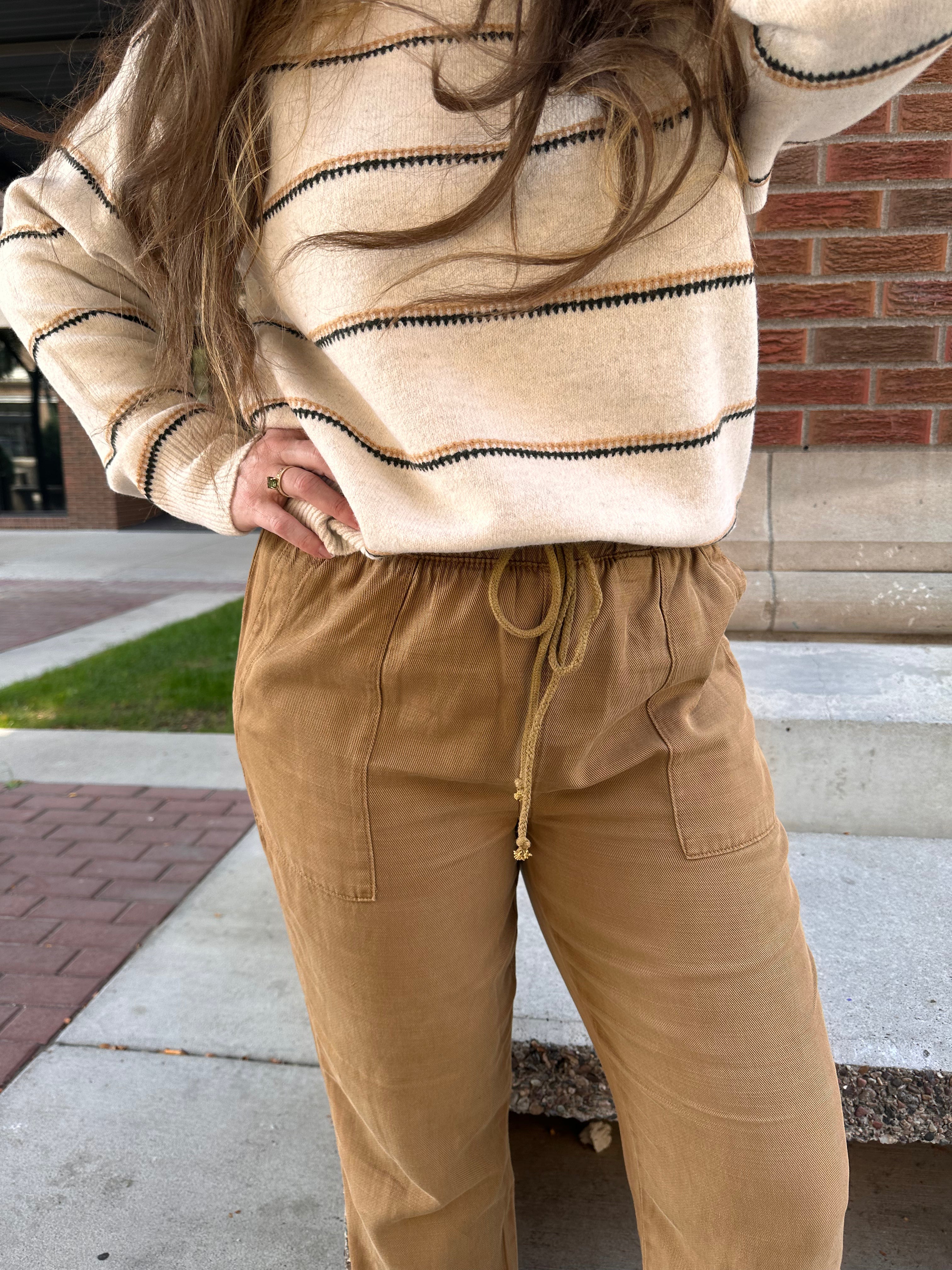 Person wearing a beige striped sweater and tan pants standing on a sidewalk.