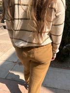 Person wearing a striped sweater and brown pants on a sidewalk