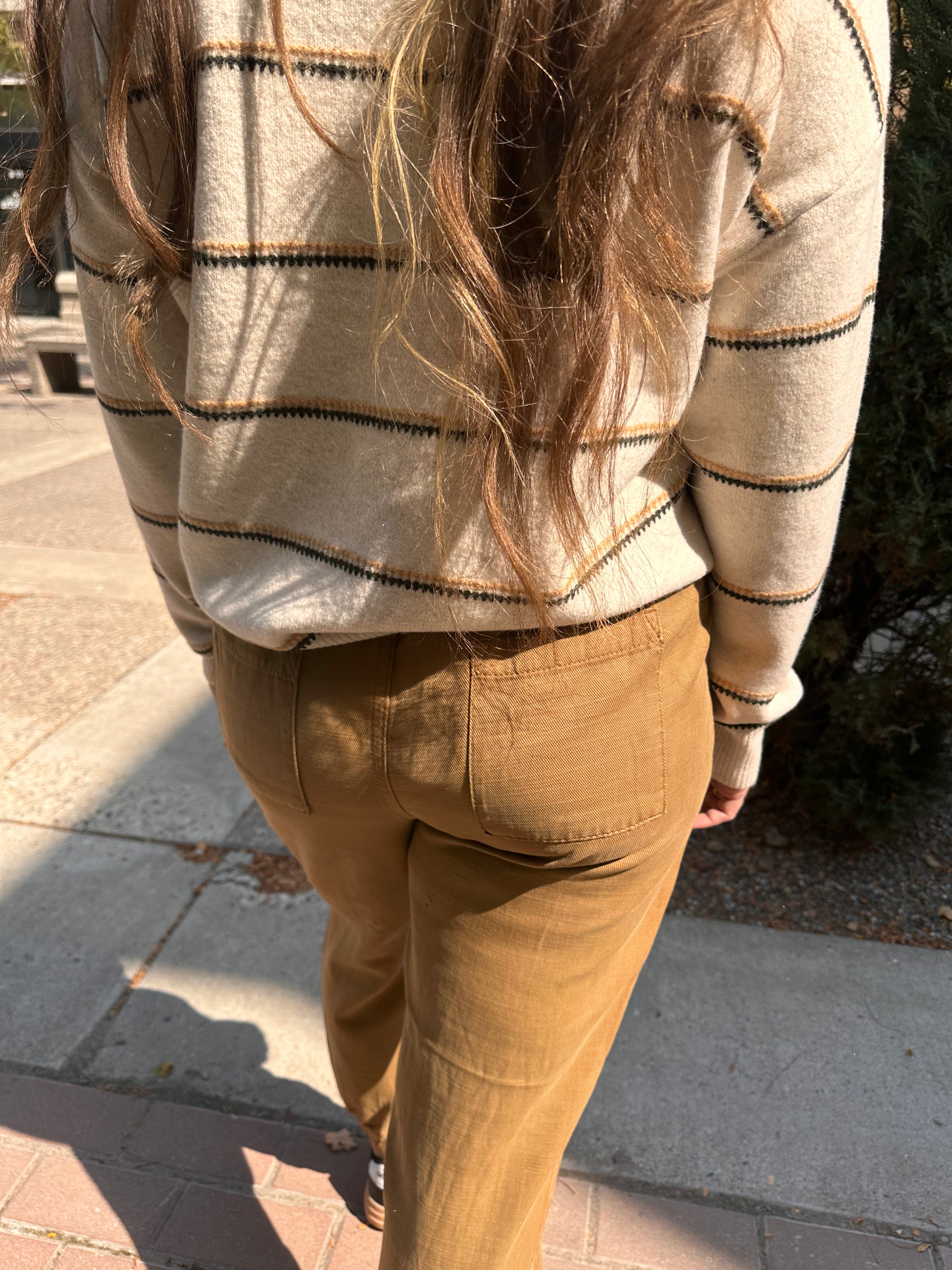 Person wearing a striped sweater and brown pants on a sidewalk