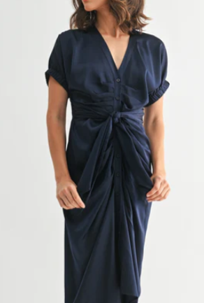 woman wearing a navy blue dress with buttons and a tie on the front with a white background