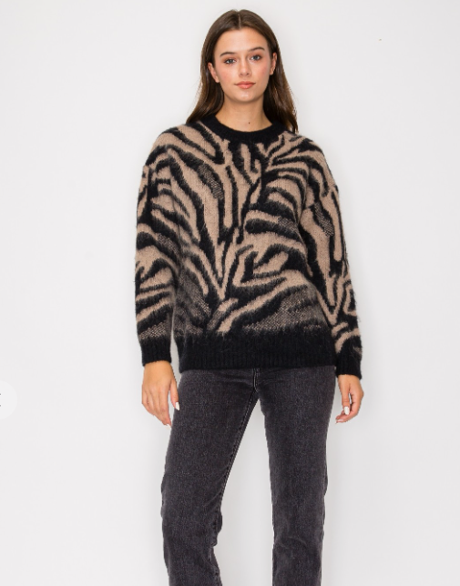 a knit sweater with beige and black zebra like designs on a woman wearing grey jeans