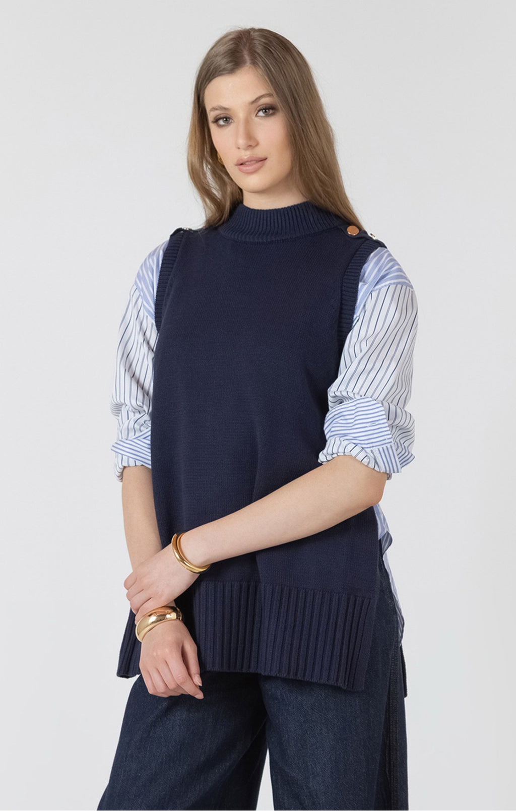 Woman wearing a navy sweater vest over a striped shirt on a white background