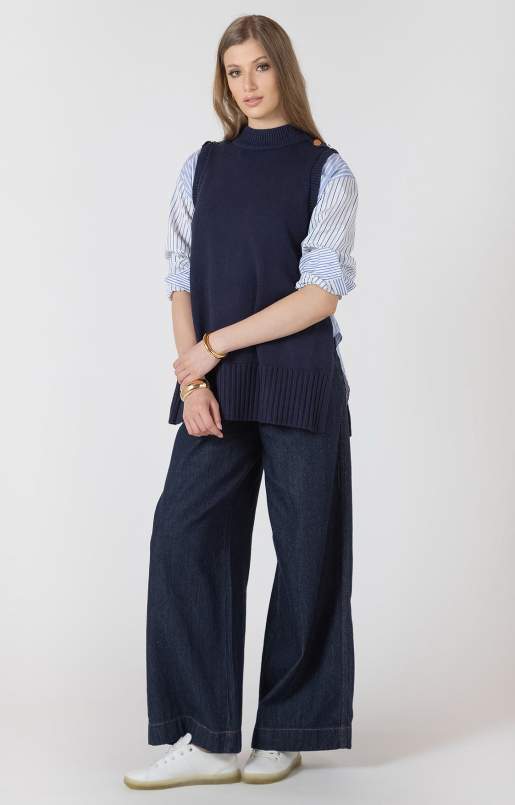 Woman wearing a navy sleeveless top, striped shirt, and wide-leg pants on a white background