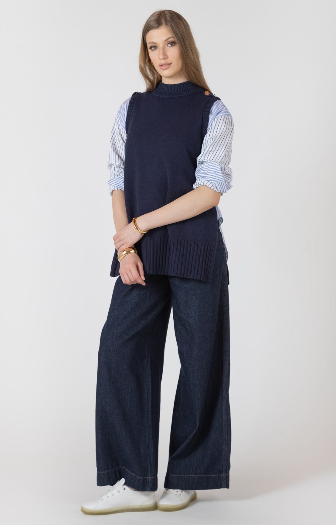 Woman wearing a navy sleeveless top, striped shirt, and wide-leg pants on a white background
