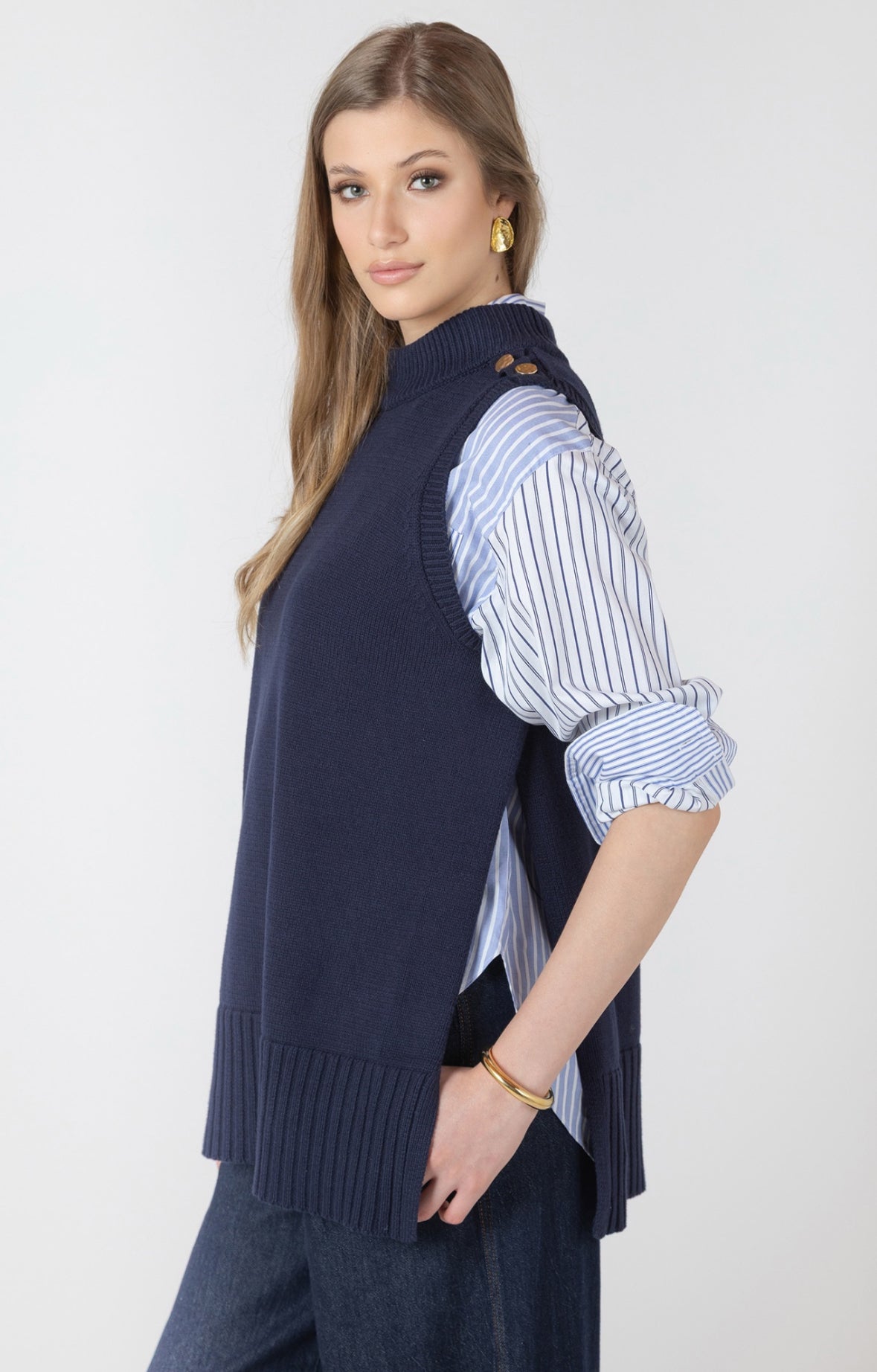 Woman wearing a navy sweater vest over a striped shirt on a white background